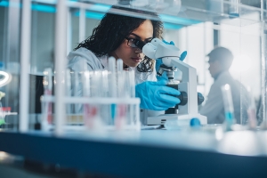Frau forscht im Labor und schaut durch Mikroskop